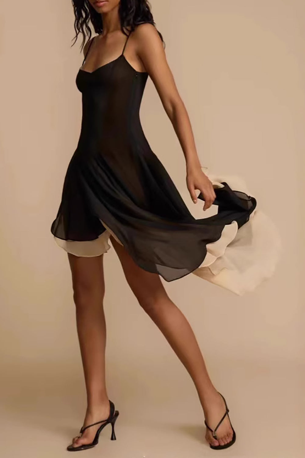 Woman wearing a black and cream asymmetrical chiffon dress with spaghetti straps, twirling the skirt to the side.