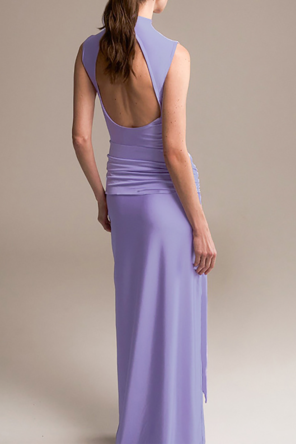 back view of a woman in a lavender sleeveless mock neck floor-length gown with an open back
