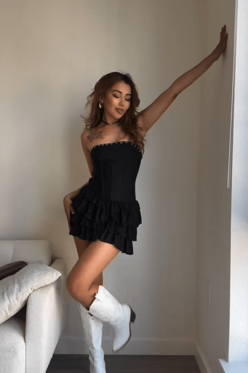 Woman in a black strapless mini dress with a ruffled skirt, posing with arm raised.