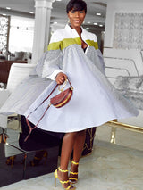 Woman wearing a white and blue striped oversized shirt dress with green color blocking on the shoulders, standing and twirling in a modern interior.