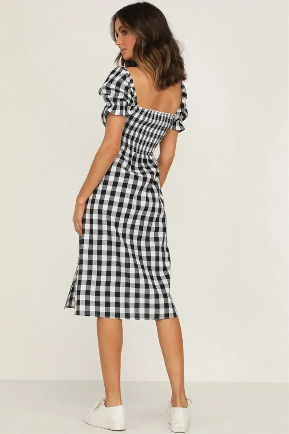 Back view of a woman wearing a black and white gingham check midi dress with puff sleeves and a square neckline.