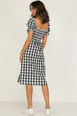 Back view of a woman wearing a black and white gingham check midi dress with puff sleeves and a square neckline.