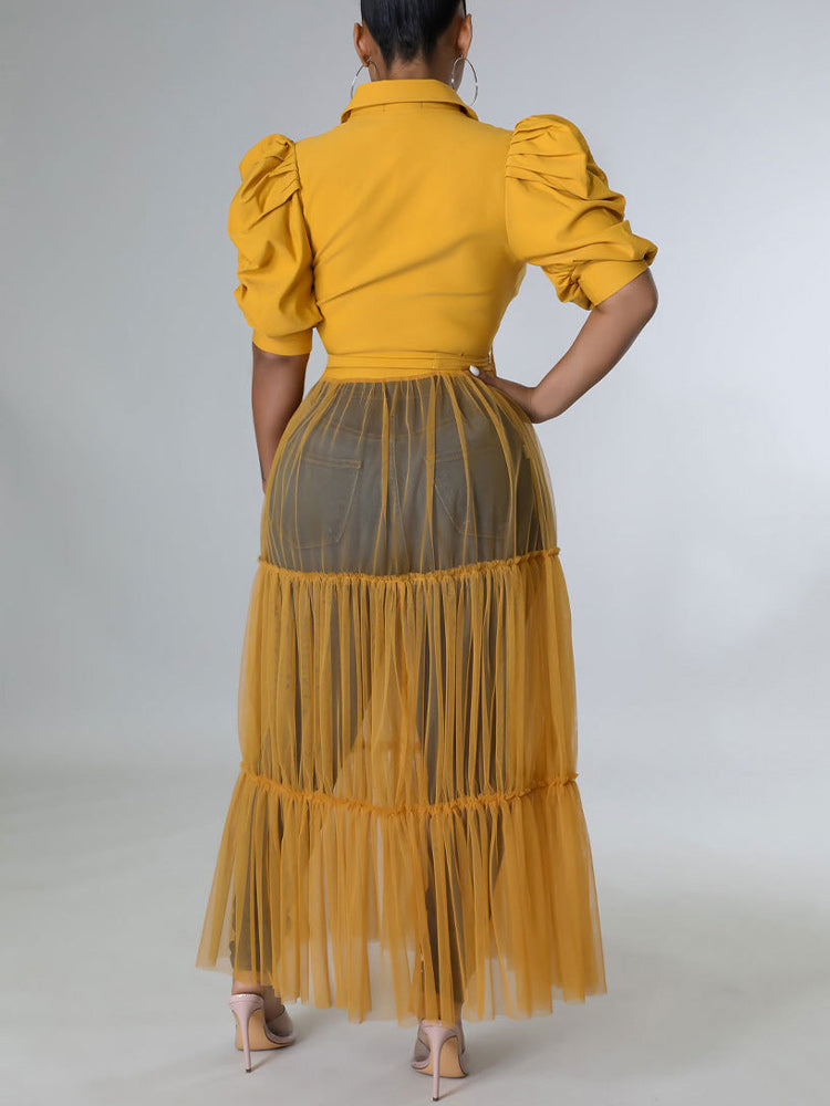 Side view of a woman wearing a mustard yellow maxi dress with puffed sleeves and a tiered tulle skirt
