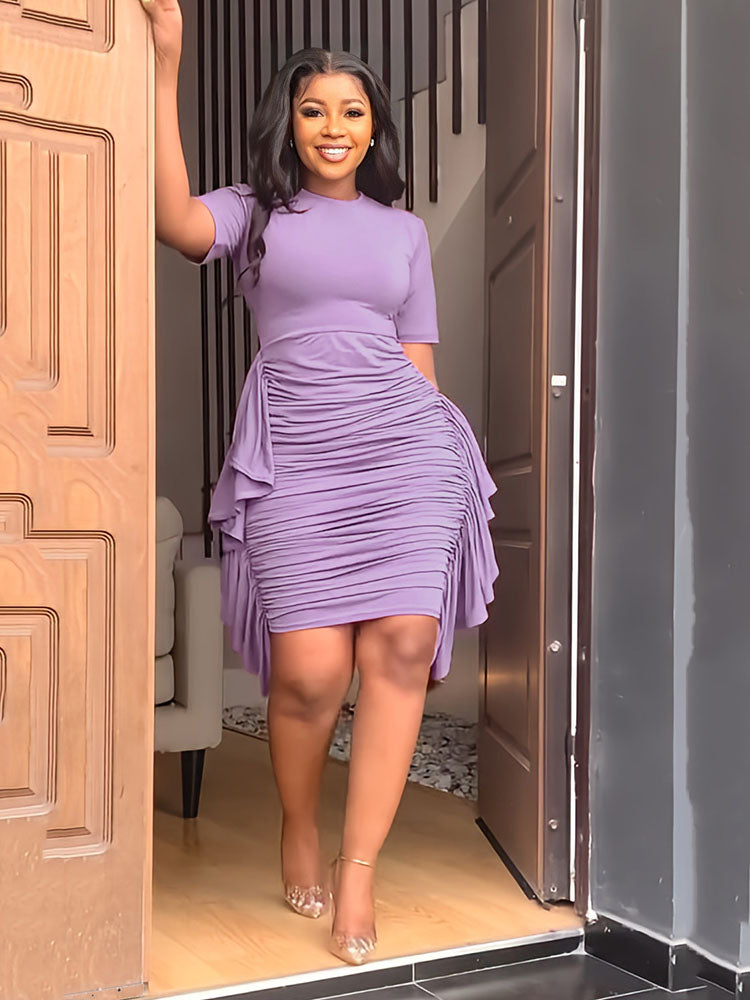 Woman in a purple ruched dress smiling and standing in a doorway.