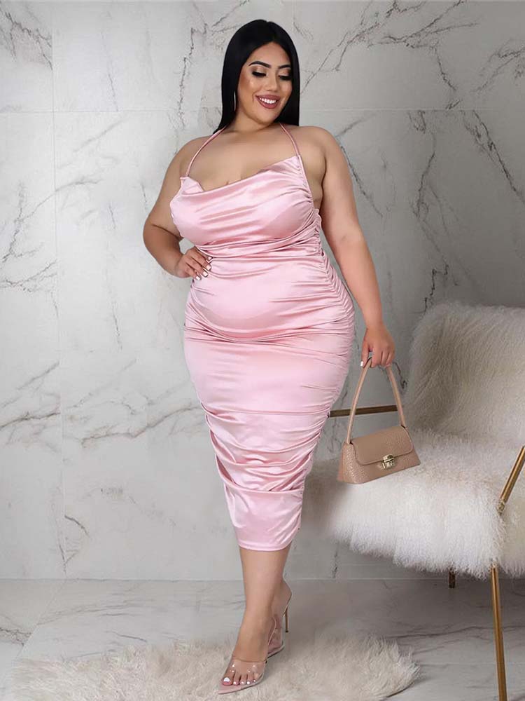 Woman wearing a pink satin ruched halter neck sheath dress and clear heeled sandals, holding a beige handbag.