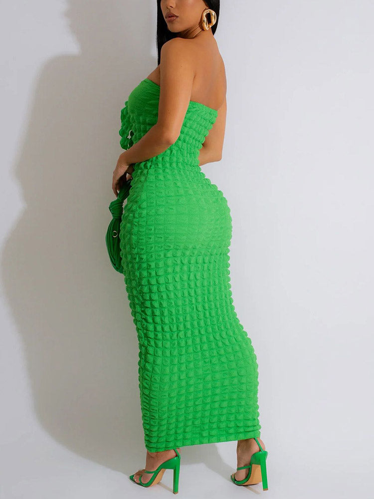 Woman from the side wearing a strapless green midi dress with textured fabric and ruched detailing at the bust, holding a green clutch bag and wearing green strappy heels.