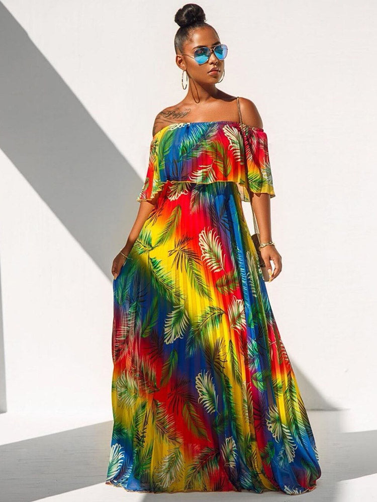 Woman wearing a vibrant rainbow gradient off-the-shoulder maxi dress with a tropical leaf print, standing against a white wall with shadows.