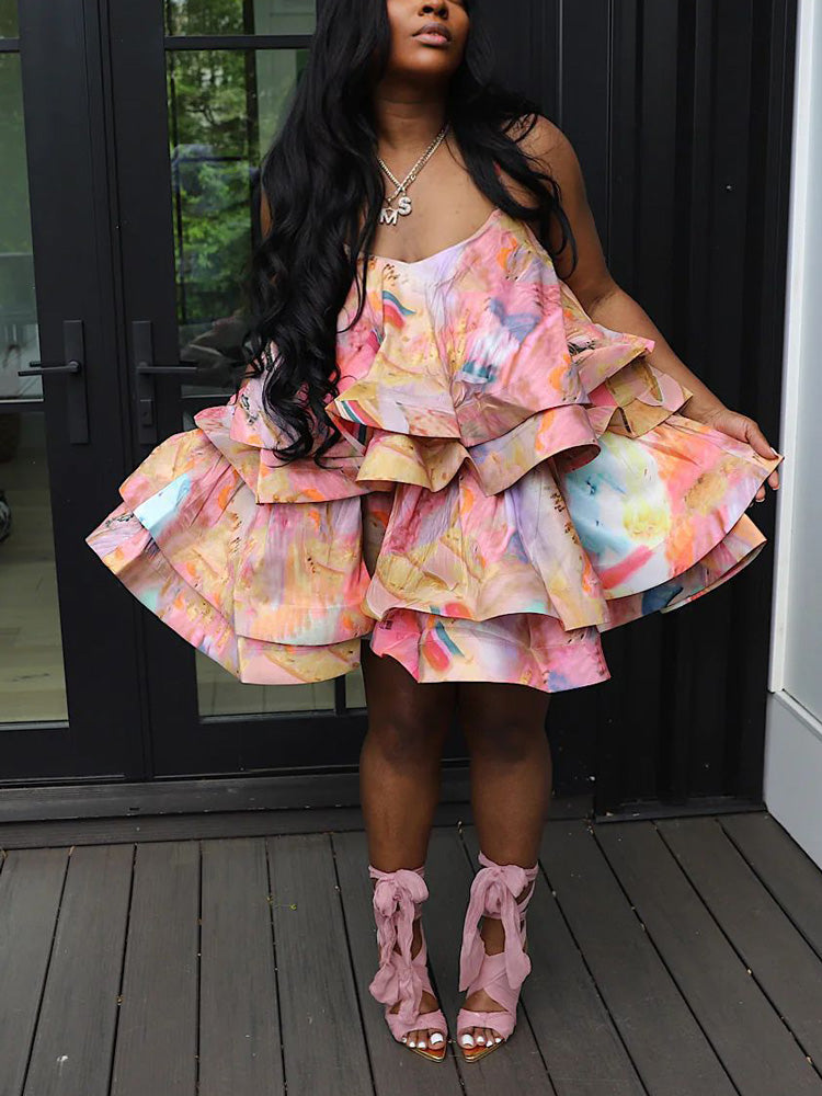 Full shot of a woman in a tiered ruffle dress with a colorful abstract pattern and pink ankle-strap heels.