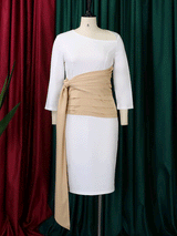 White sheath dress with a tan ruched sash and tie detail displayed on a mannequin against a backdrop of burgundy and green curtains.
