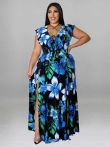 Woman wearing a black maxi dress with a blue and green floral print, featuring a V-neck with lace-up detail and a high slit.