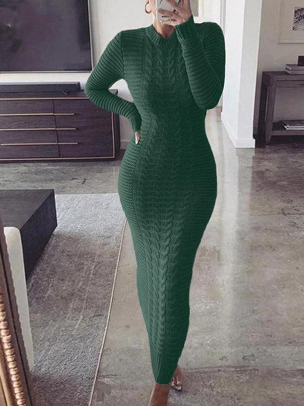 Woman wearing a long green cable knit dress with long sleeves and a mock neck standing in a living room.