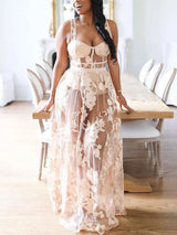 Woman in a sheer floral embroidered maxi dress with a corset-style bodice, leaning on a dining table.