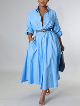 Woman wearing a light blue collared shirt dress with a cinched waist and rolled sleeves.