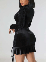 Side view of a woman showcasing the silhouette of a black velvet ruched dress.