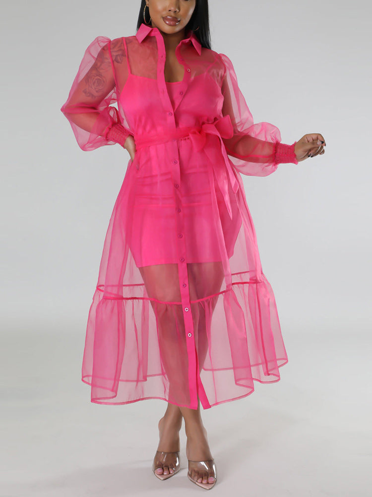 Woman wearing a sheer pink organza dress over a pink slip dress, belted at the waist with puff sleeves and a tiered hem.