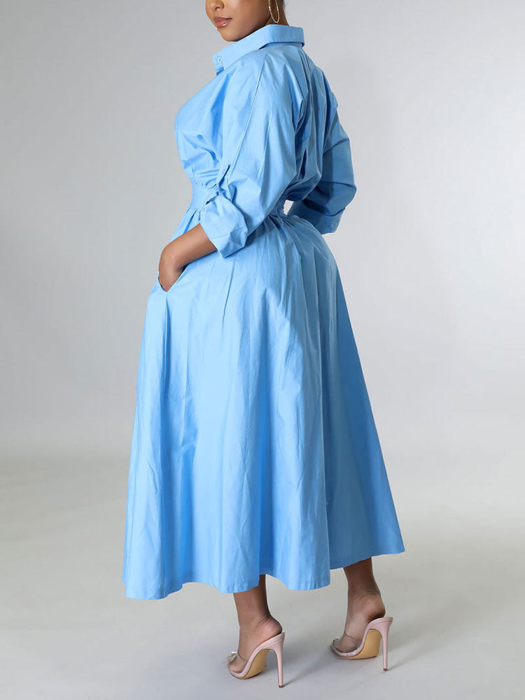 Back view of a woman in a light blue A-line shirt dress with pockets.