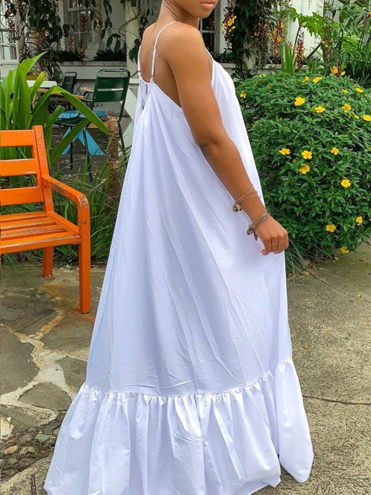 Side view of a woman in a white maxi dress with ruffled hem and spaghetti straps.