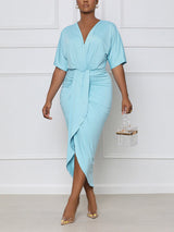 Front view of a woman wearing a light blue V-neck wrap dress with short sleeves, ruched waist, and asymmetrical hem with a slit.