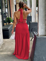 Back view of a woman in a red halter neck maxi dress with an open back and tiered skirt.