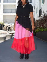 Woman wearing a black short-sleeved dress with a layered, color-blocked mesh skirt in pink and red hues, paired with black boots.