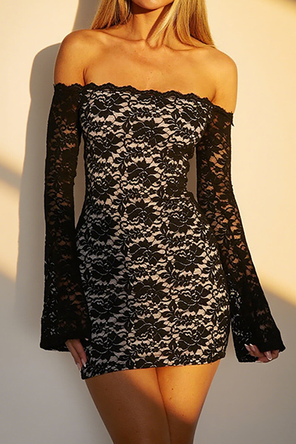 Woman wearing a black and white lace off-the-shoulder mini dress with long bell sleeves.