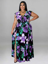 Woman wearing a black maxi dress with a purple and green floral print, featuring a V-neck with lace-up detail and a high slit.