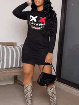 Full-body shot of a woman in a black long-sleeve hooded mini dress with a graphic smiley face print and a black handbag.