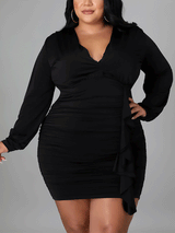 Plus-size woman wearing a black ruched mini dress with a v-neck and long sleeves, shown from the front.