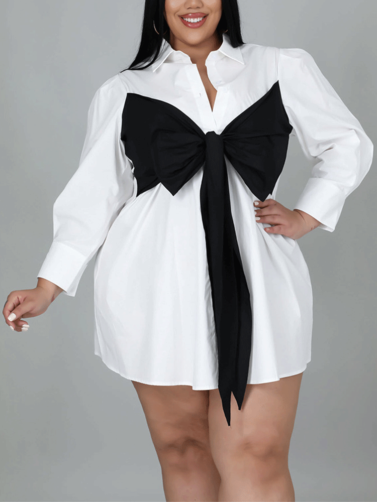 Plus-size woman wearing a white shirt dress with a black oversized bow detail on the front.