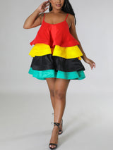 Woman wearing a red, yellow, black, and teal tiered mini dress with spaghetti straps and black ankle-strap heels.