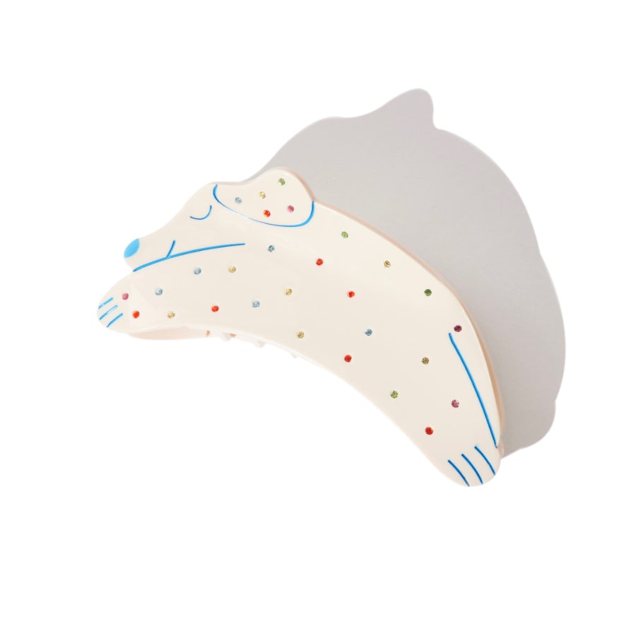 Cream dog-shaped hair claw with colorful polka dots and blue line details, casting a shadow.