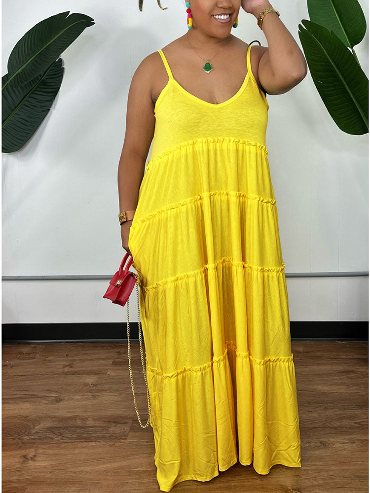 Woman wearing a yellow tiered maxi dress with spaghetti straps and a v-neckline, holding a red handbag.