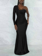 Woman wearing a floor-length, one-shoulder black dress with a long sleeve on the left side and a mermaid hem, standing against a marbled background.