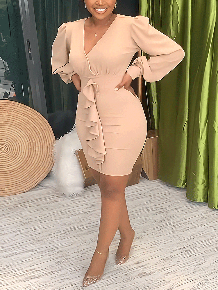 Woman posing in a beige sheath dress with long puff sleeves and ruffle detailing.