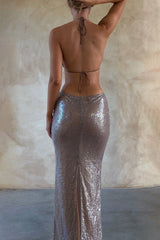 Back view of a woman in a long, sequined, taupe halter dress.