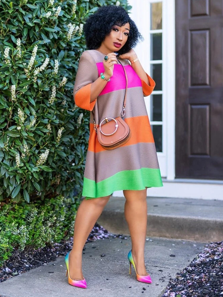 A woman in a vibrant colorblock dress smiles and touches her hair.