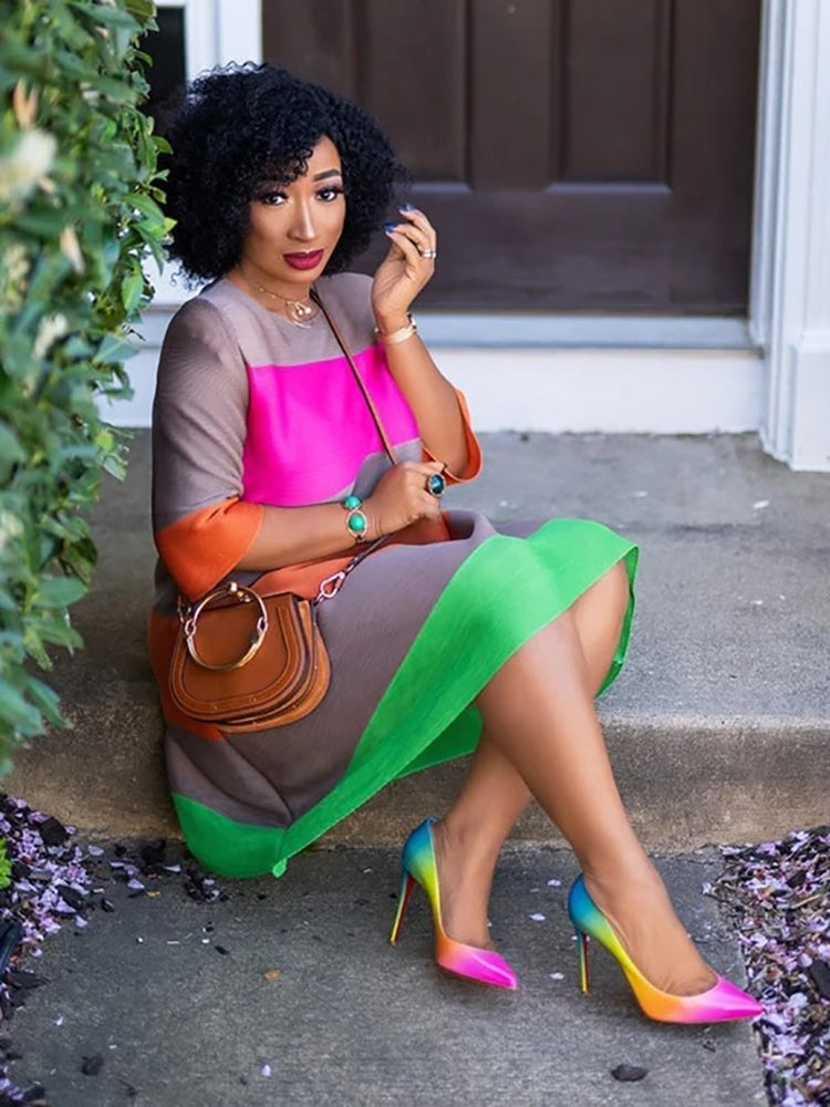 A woman sits on steps wearing a pleated colorblock dress and high heels.