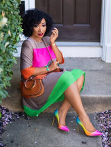 A woman sits on steps wearing a pleated colorblock dress and high heels.