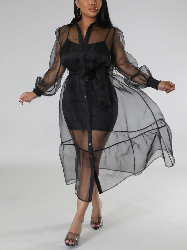 Woman wearing a sheer black organza dress over a black slip dress, belted at the waist with puff sleeves and a tiered hem.