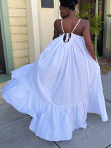 Back view of a woman in a white maxi dress with ruffled hem and tie detail at the back.