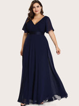 Plus-size woman in a navy blue chiffon formal dress with flutter sleeves and a V-neckline, posing against a neutral background.