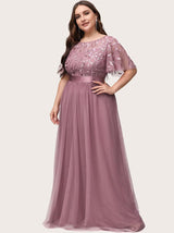 Side profile of a woman in a dusty rose A-line maxi dress with embroidered flutter sleeves and a satin waistband.
