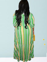 Back view of a woman wearing a green, yellow, and white striped maxi dress with a belted waist.