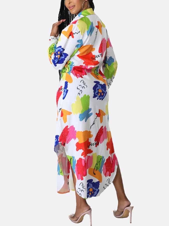 Back view of a woman wearing a long, white, collared shirt dress with a colorful abstract print. The dress features long sleeves, a button-down front, and a high-low hemline with side slits.