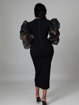 Rear view of a woman in a black midi dress with sheer puff sleeves