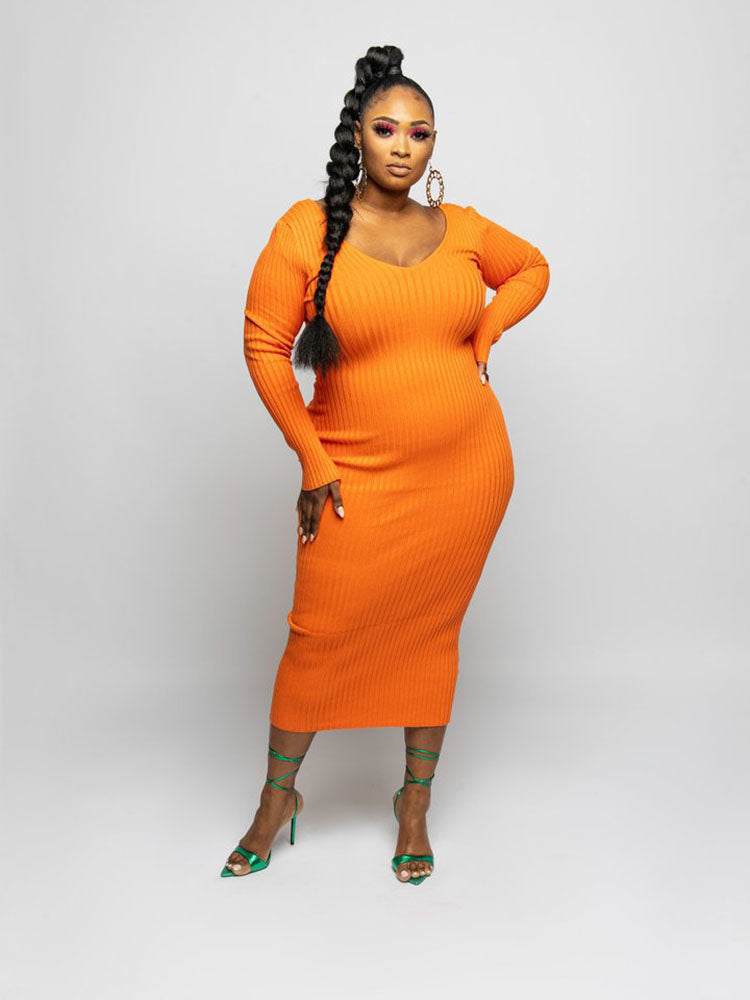 Woman wearing an orange ribbed knit midi dress with long sleeves and a V-neckline, with a braid and green strappy heels.