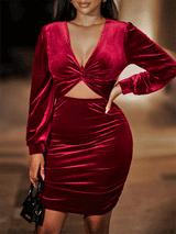 Woman wearing a deep red velvet bodycon dress with a v-neck, twist front detail, cut-out waist, ruched skirt, and long sleeves.