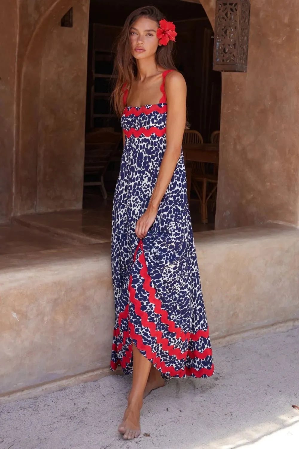Woman in a blue and white animal print maxi dress with red scalloped trim, lifting the hem of the dress slightly.