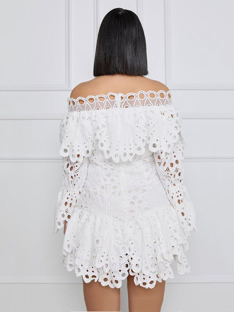 Back view of a woman wearing a white off-the-shoulder eyelet lace mini dress with bell sleeves and ruffled tiers, standing against a white wall.