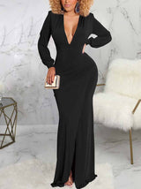 Woman wearing a long black dress with a deep V-neckline, long sleeves, ruched detailing, and a high slit.